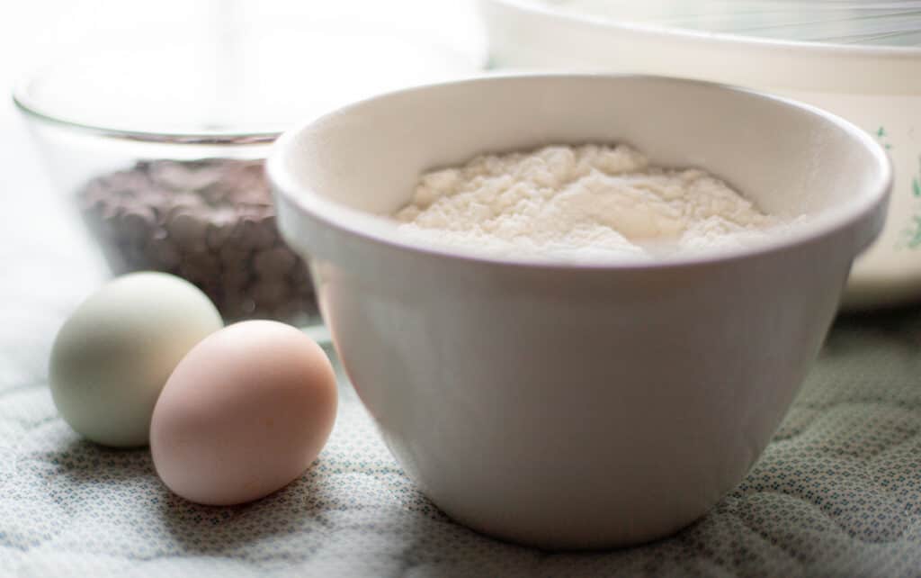 Flour and chocolate chips in mixing bowls with eggs