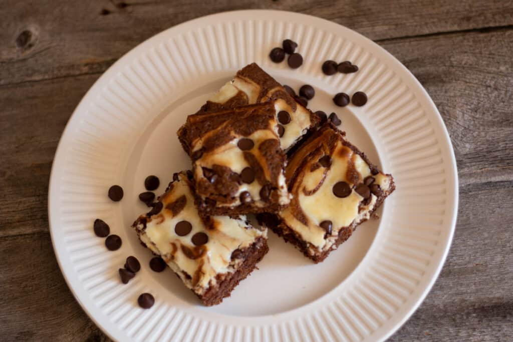 cream cheese brownies on white plate with chocolate chips sprinkled around the plate