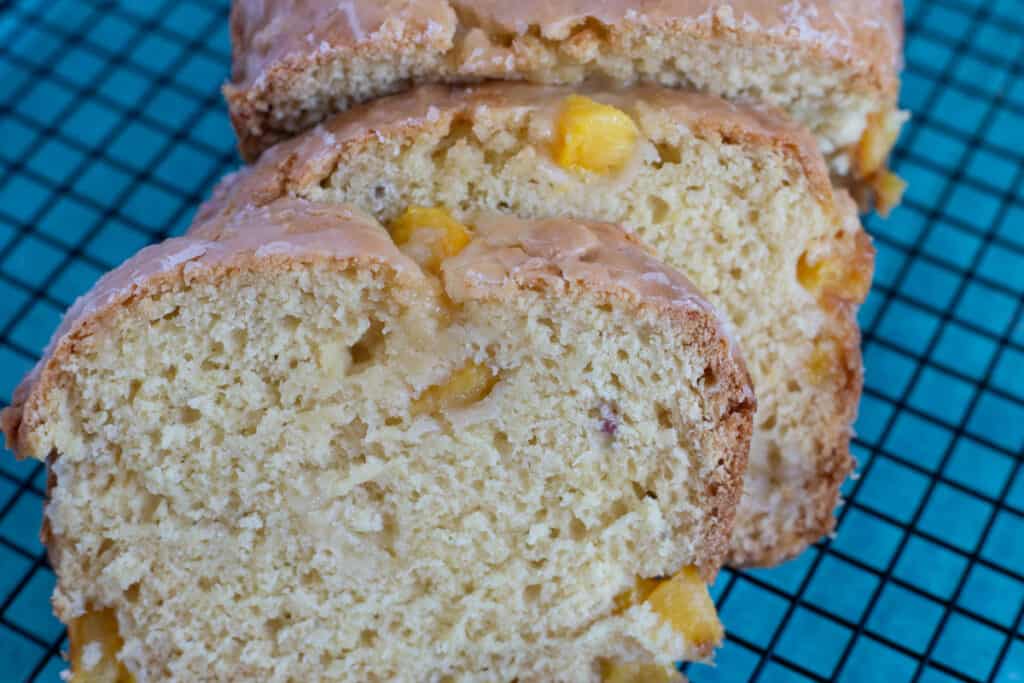 Peach Bread sliced with the remainder of the loaf sitting behind the slices. The slices and loaf are sitting on a wire cooling rack with a blue cloth under it.