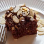 A piece of chocolate cake sitting on a white plate. There is a fork resting on the plate.