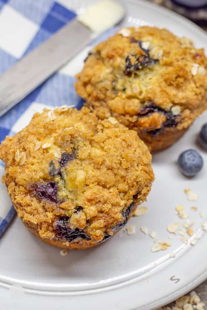 Two banana blueberry muffins on white plate with blue and white checkered napkin.