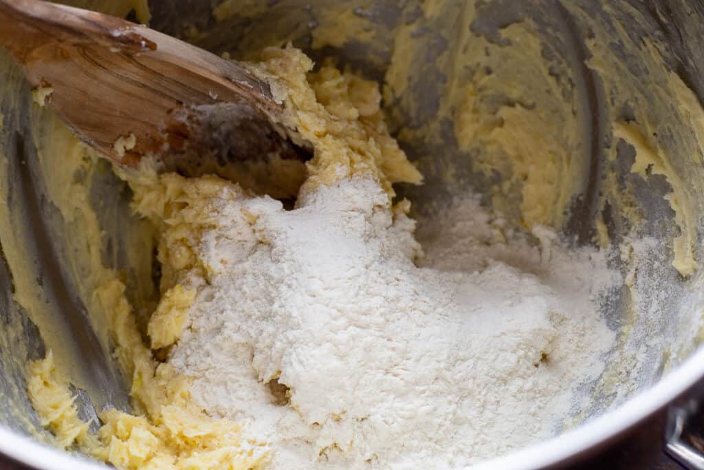 Process photo of adding in the flour by hand with a wooden spoon.