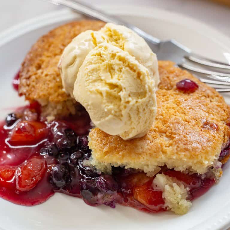 Close up image of peach and blueberry cobbler with vanilla ice cream.