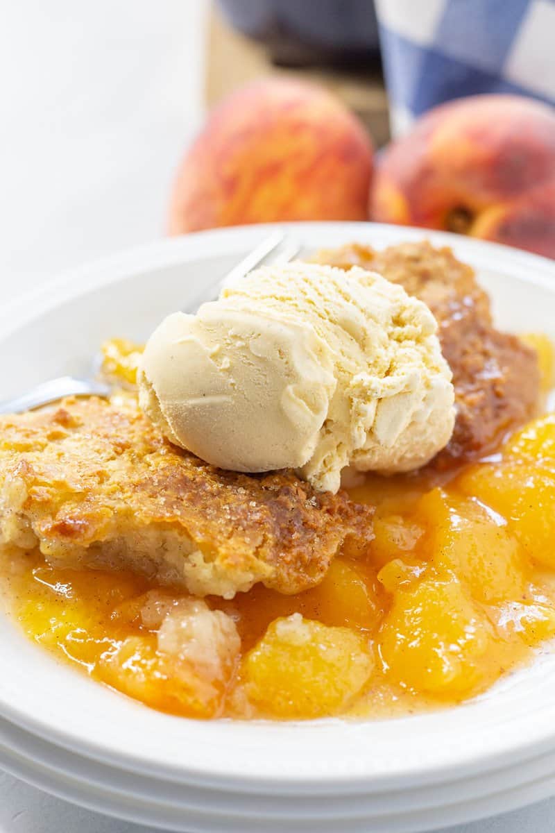 Homemade peach cobbler on a white plate with ice cream for a non traditional Thanksgiving dessert.