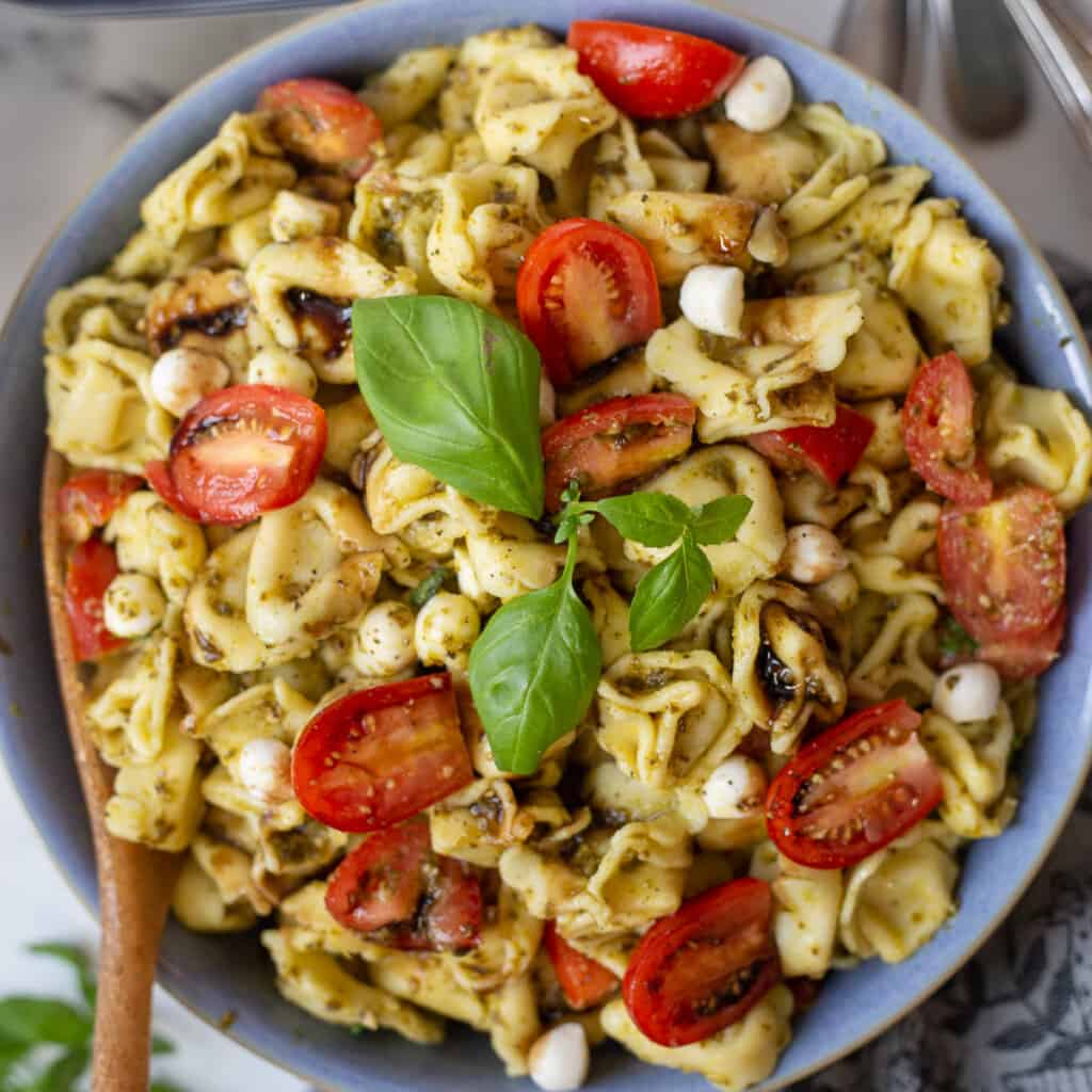Close up image of caprese pesto pasta salad in bowl.