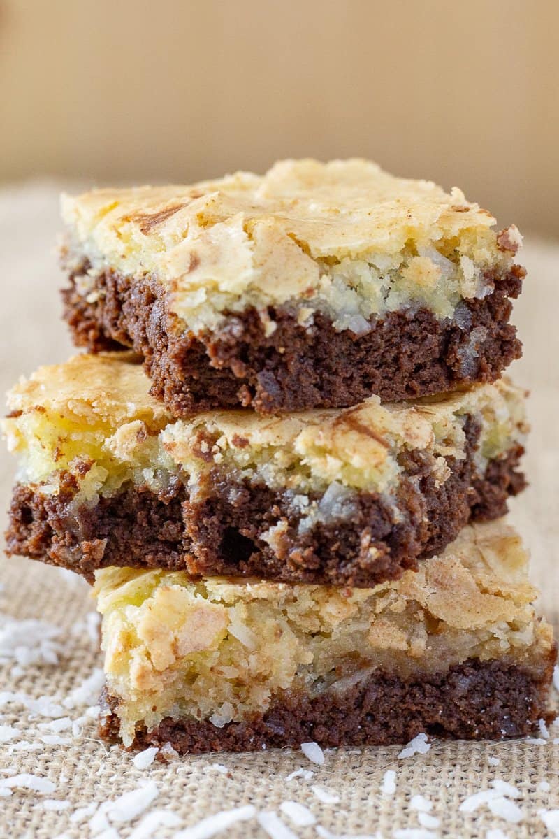 Chocolate coconut brownies sliced and stacked on a wooden board.