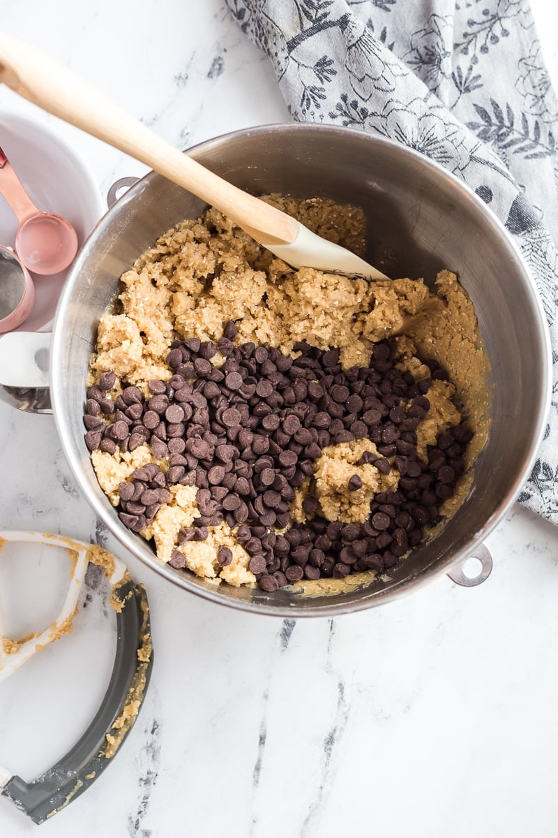 Cookie dough with chocolate chips in bowl from stand mixer with spatula.