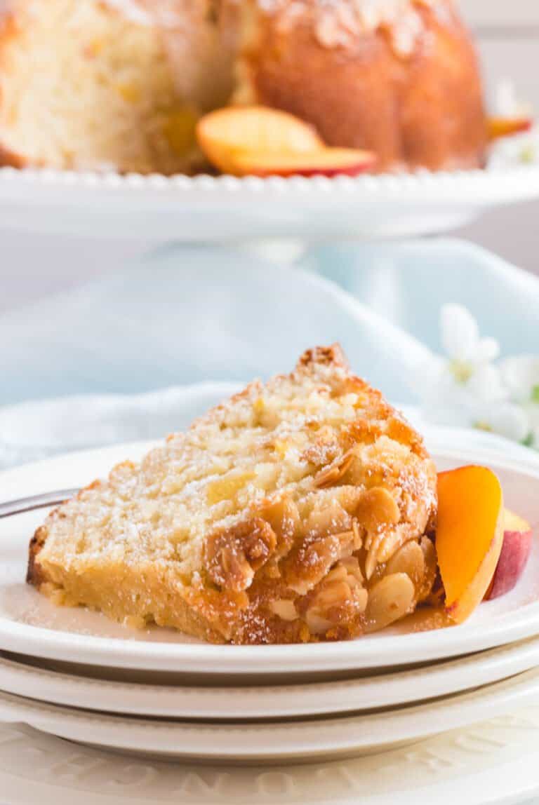 Slice of peach almond cake on white plate with remaining bundt cake in background.