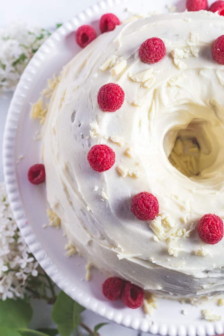 Overhead view of white chocolate raspberry bundt cake, garnished with fresh raspberries and grated white chocolate.
