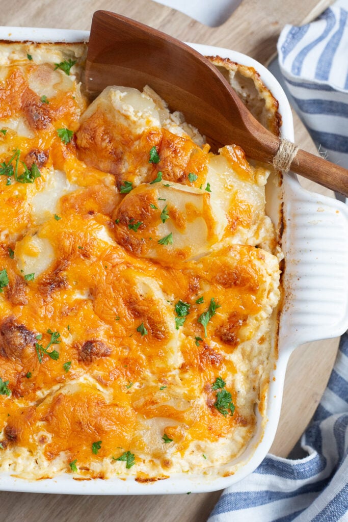 Smoked Gouda potatoes au gratin in baking dish with wooden spoon.