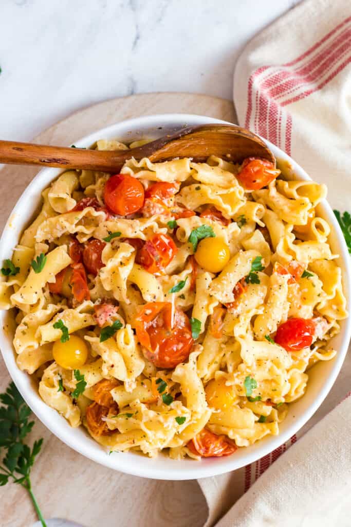 Creamy Boursin cheese pasta with cherry tomatoes in white bowl with wooden spoon.