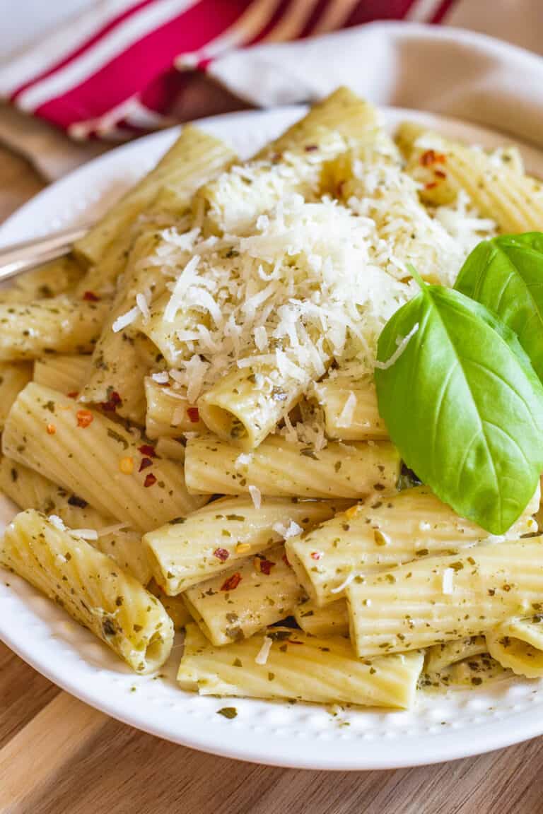 Creamy pesto pasta on white plate with fresh Parmesan cheese and fresh basil.