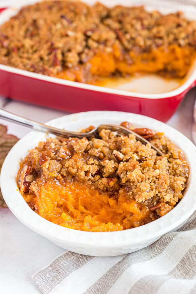 Serving of sweet potato casserole in small white bowl with fork.