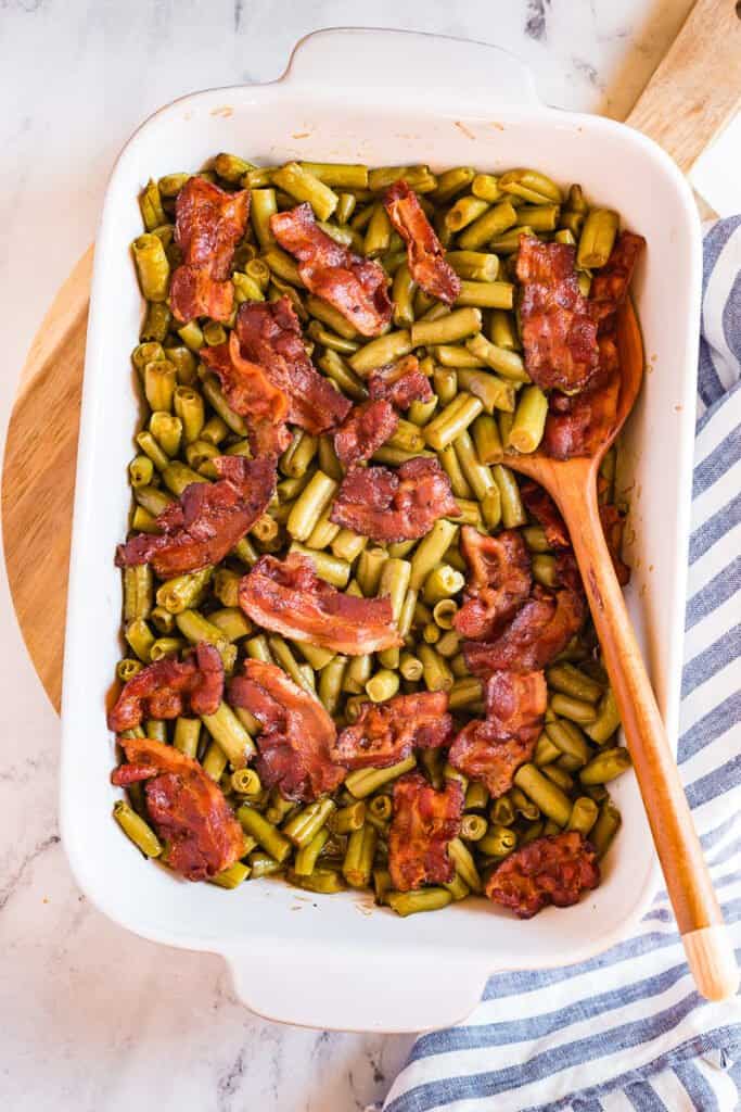 Crack green bean casserole in white baking dish with spoon.