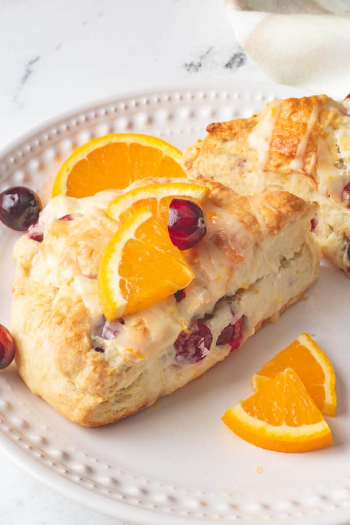 Cranberry orange scones on white plate with orange slices.