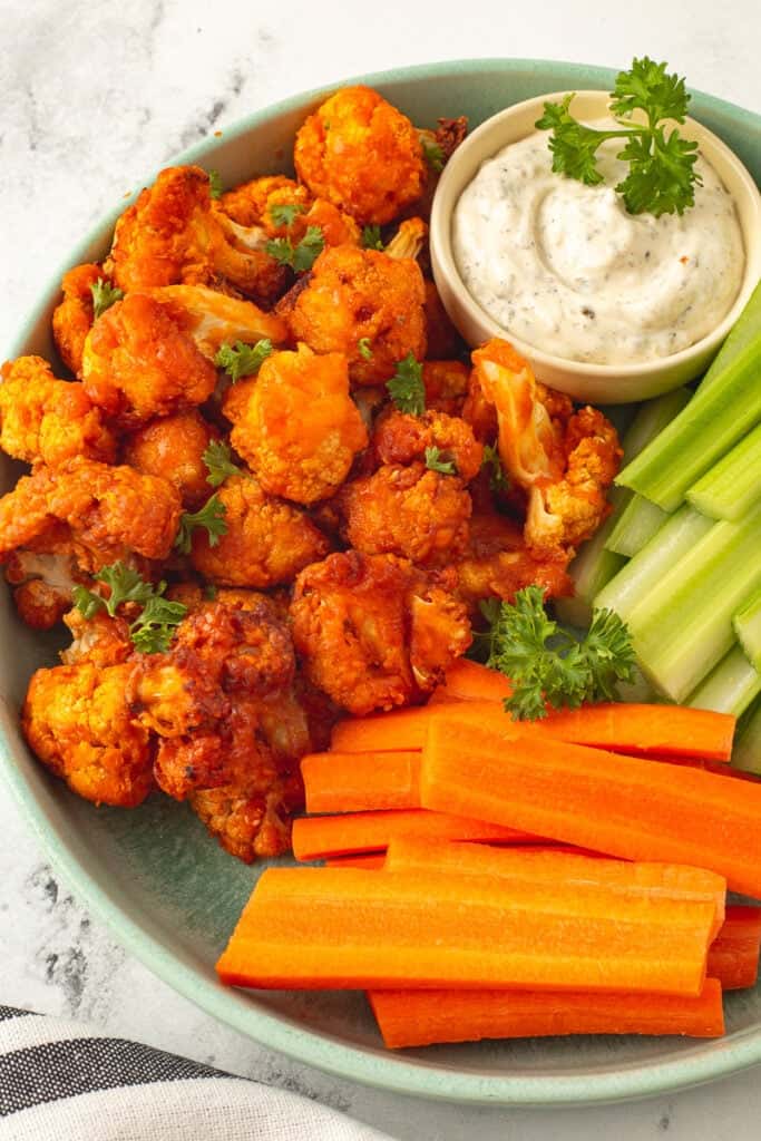 Air fryer buffalo cauliflower bites on a green plate with carrots, celery and dip.