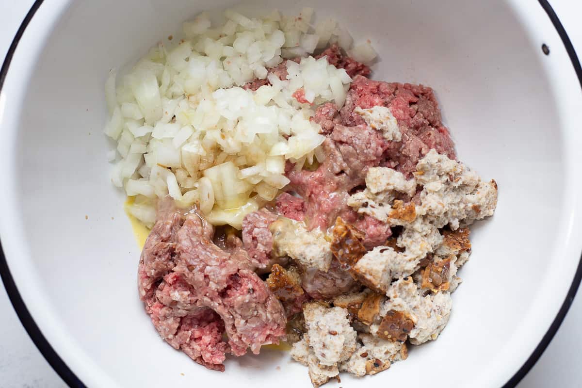 Ground beef, ground pork, worcestershire sauce, onions, egg and milk in small bowl ready to be mixed.