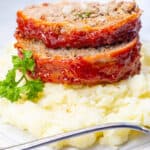 2 slices of bacon wrapped meatloaf on top of mashed potatoes.