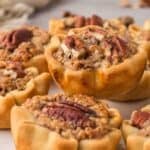 Mini pecan pies stacked on a white plate.