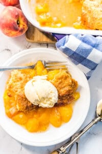 Peach cobbler with vanilla ice cream on a white plate with a fork.