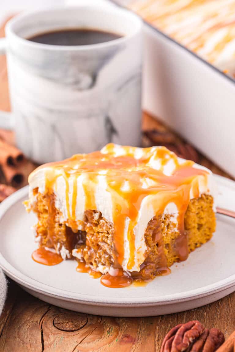 Pumpkin caramel poke cake on plate with cup of coffee in the background.