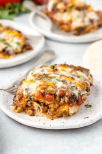 Beef enchilada casserole on a white plate with a fork.