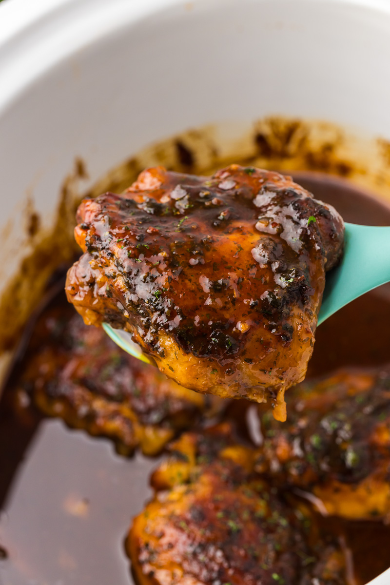 Crockpot bbq chicken thighs held up on a spoon.