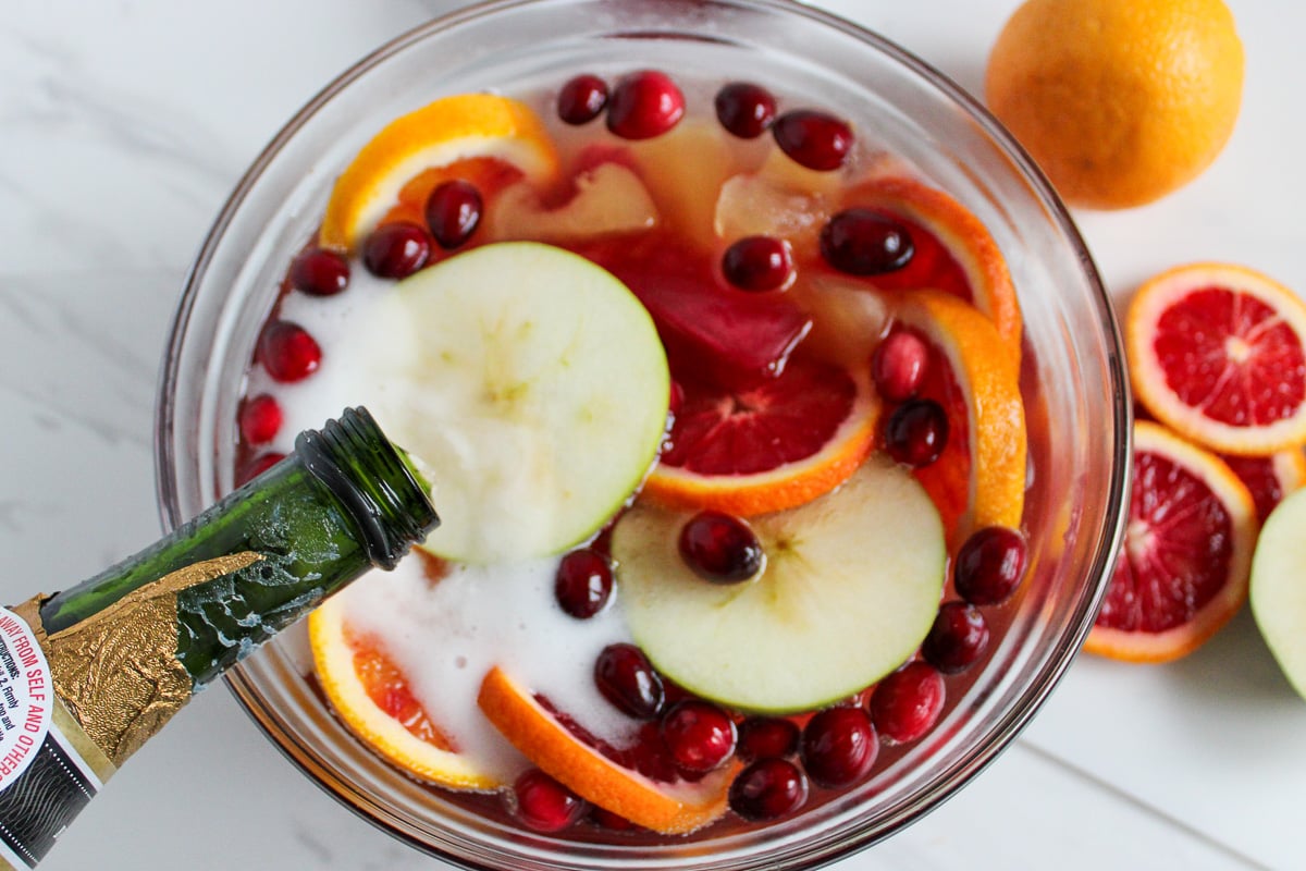 Champagne is poured into the fruit and juice mixture in glass bowl.