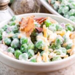 Pea salad with bacon in a white bowl.