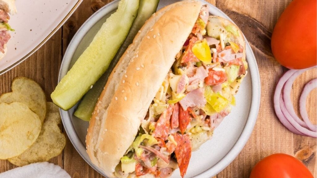 Italian sandwich served on a plate with pickles on the side.