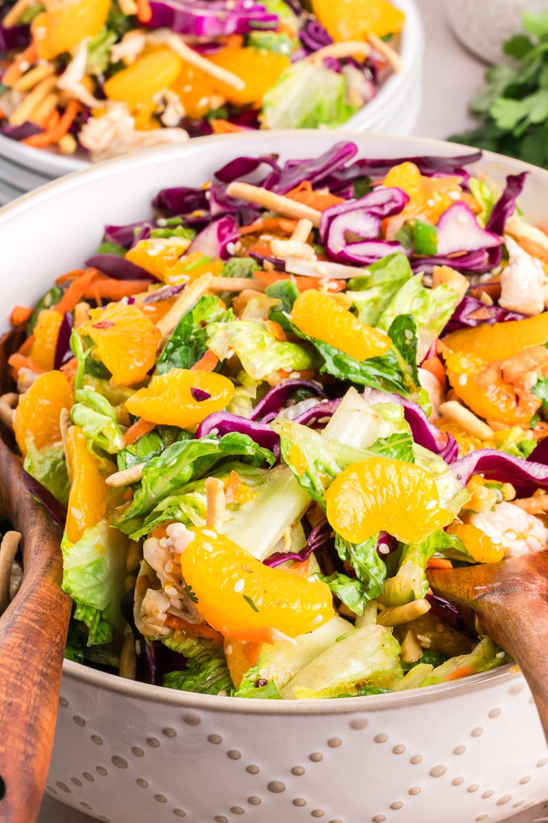 Finished dish of Chinee chicken salad with mandarins in a bowl with wooden serving spoons.