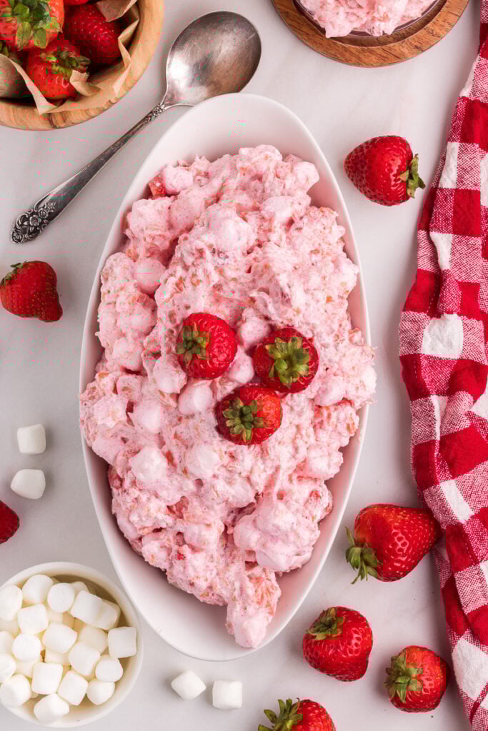 Strawberry fluff salad in a white bowl with fresh strawberry garnish.
