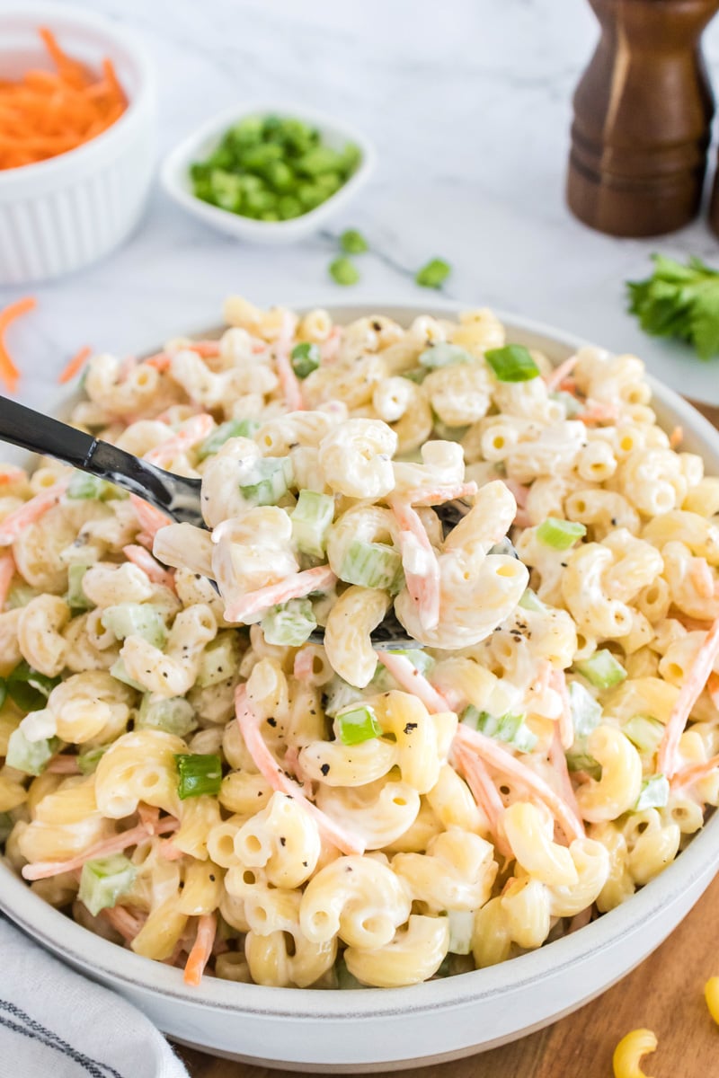 Hawaiian macaroni salad scooped up with a spoon held over bowl.
