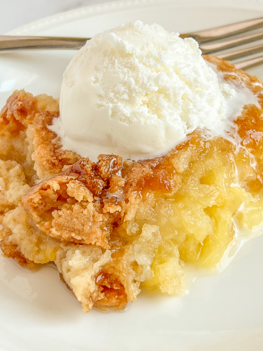 Piece of pineapple dump cake on a white plate with ice cream on top for a popular easy Thanksgiving dessert.