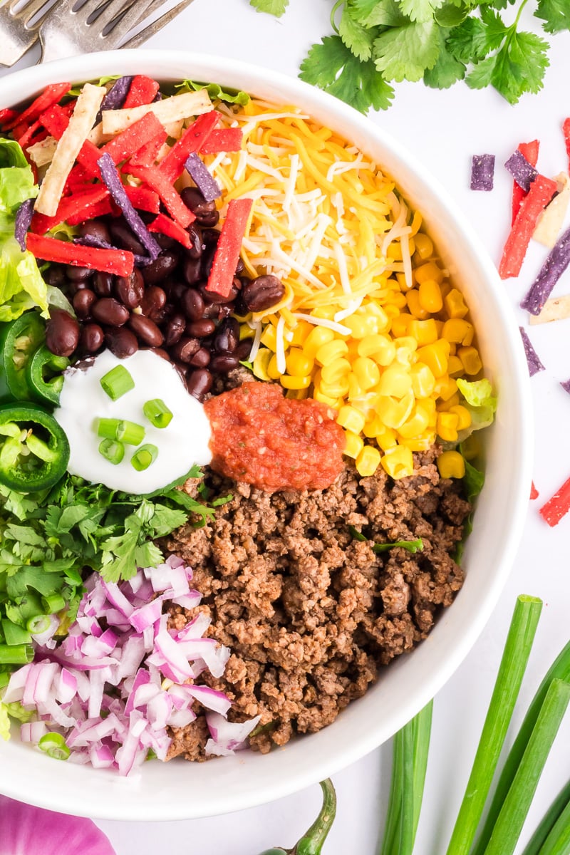 Overhead image of beef taco salad in a white bowl, ready to be tossed.