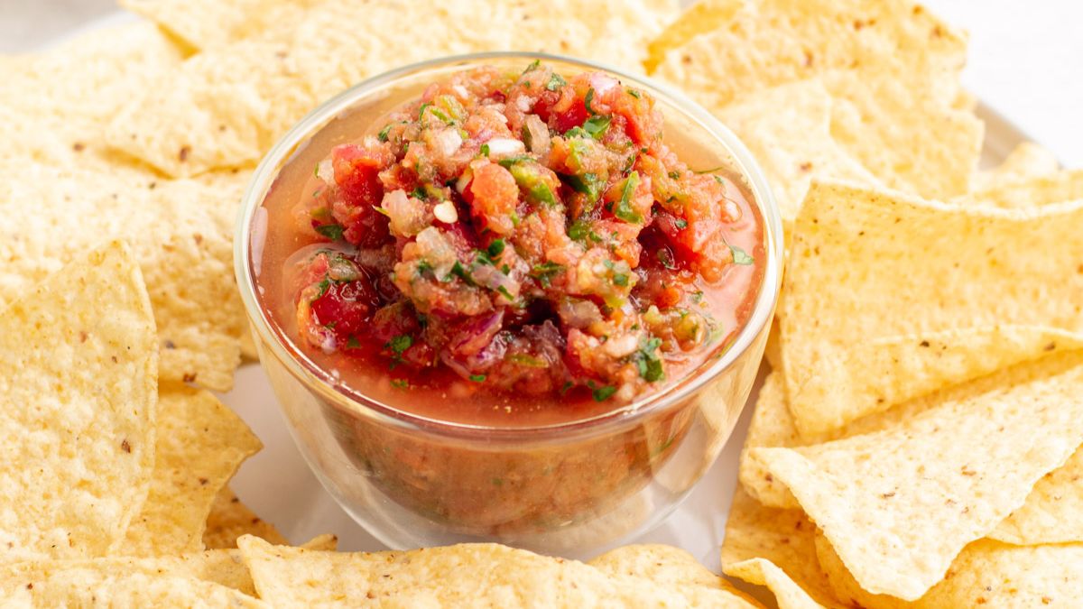 Blender salsa in a small glass bowl surrounded by nacho chips.