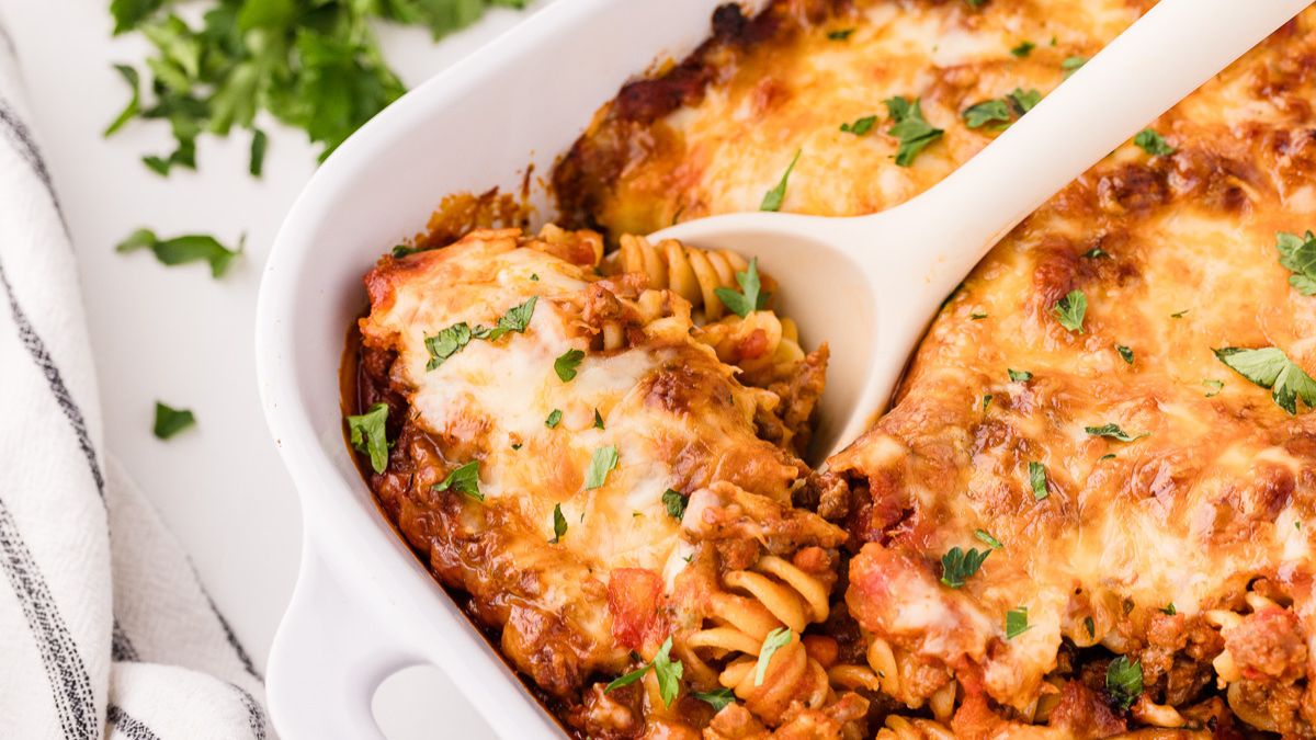 Bolognese pasta bake in white baking dish with spoon scooping up a serving.