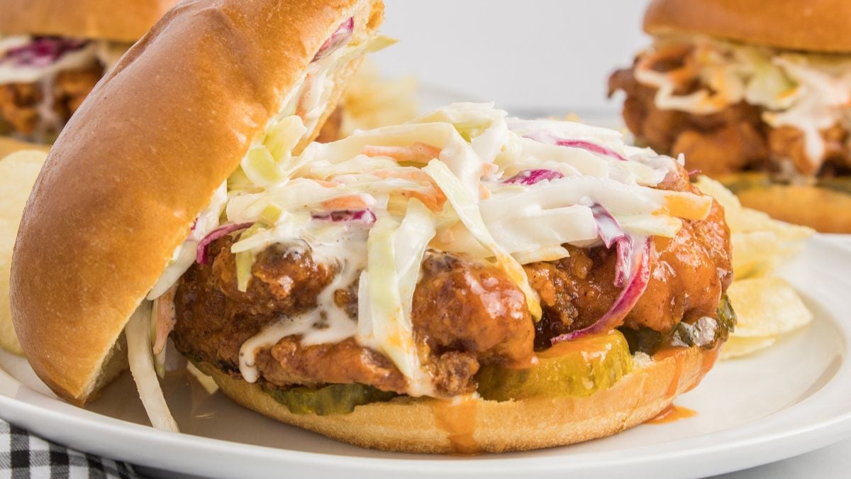 Hot honey chicken sandwich with coleslaw served on a bun and placed on a white plate.