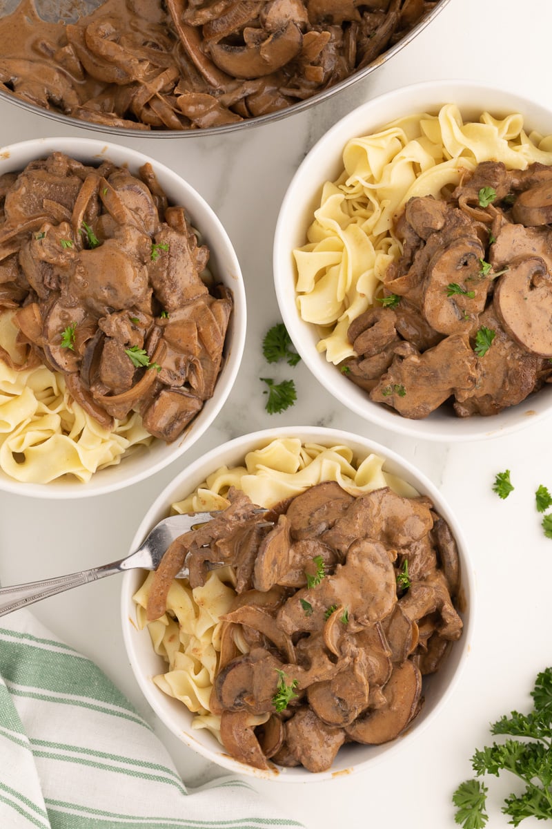 Overhead of three bowls of beef stroganoff with noodles.