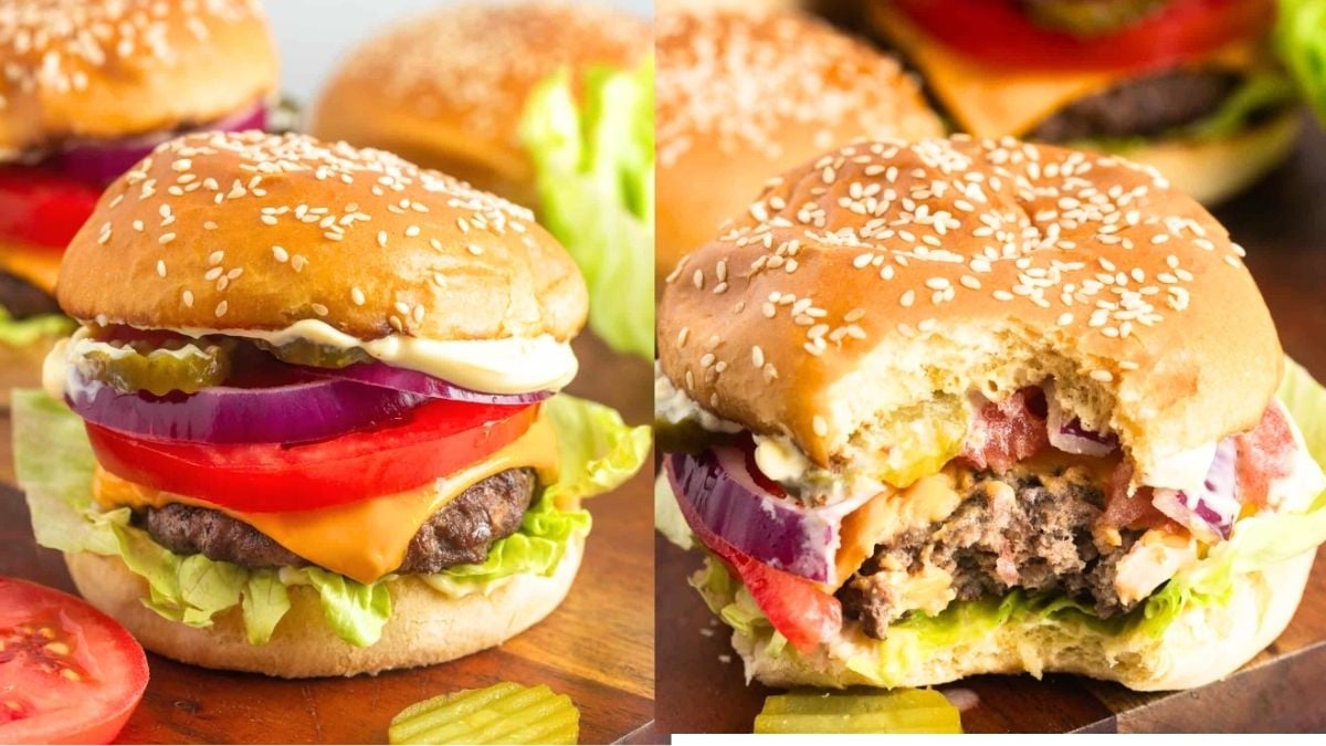 Grilled burgers on wooden board with pickles and tomatoes on the side.