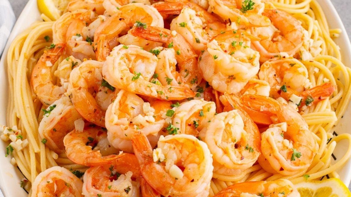 Shrimp scampi served on a bed of angel hair pasta on a white plate.