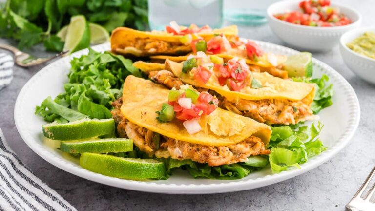 Baked chicken tacos served on a bed of leafy lettuce on a white plate.