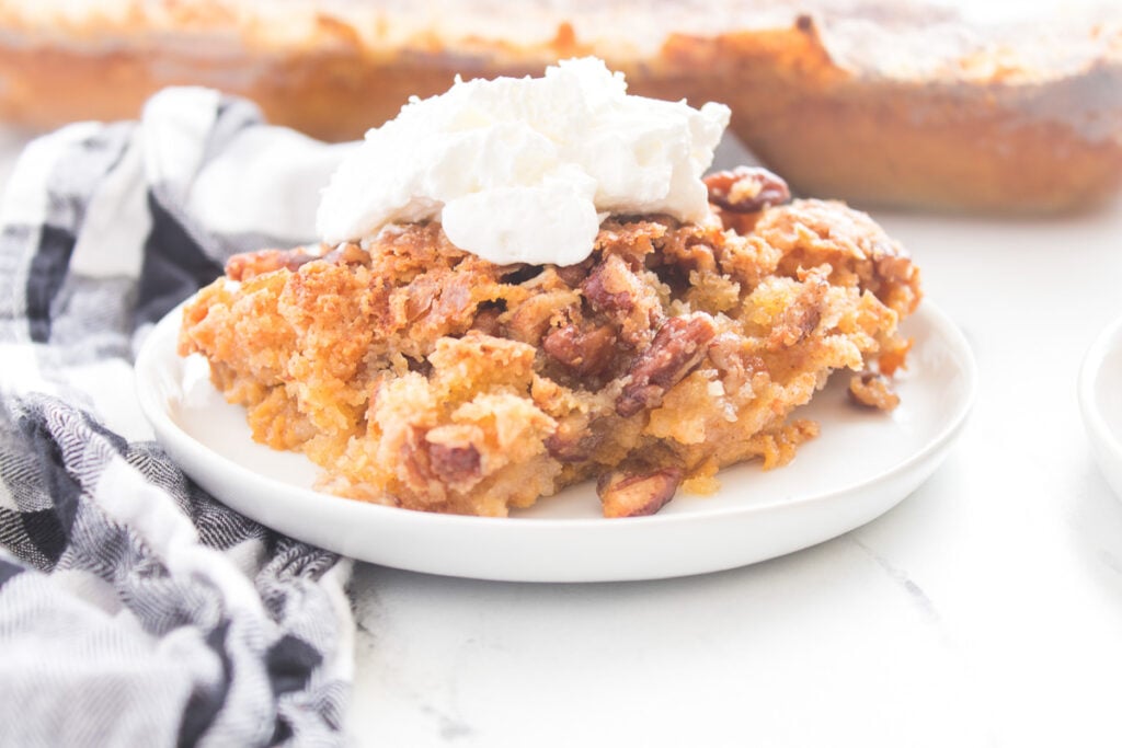Piece of pumpkin crunch cake on a white plate with whipped cream.