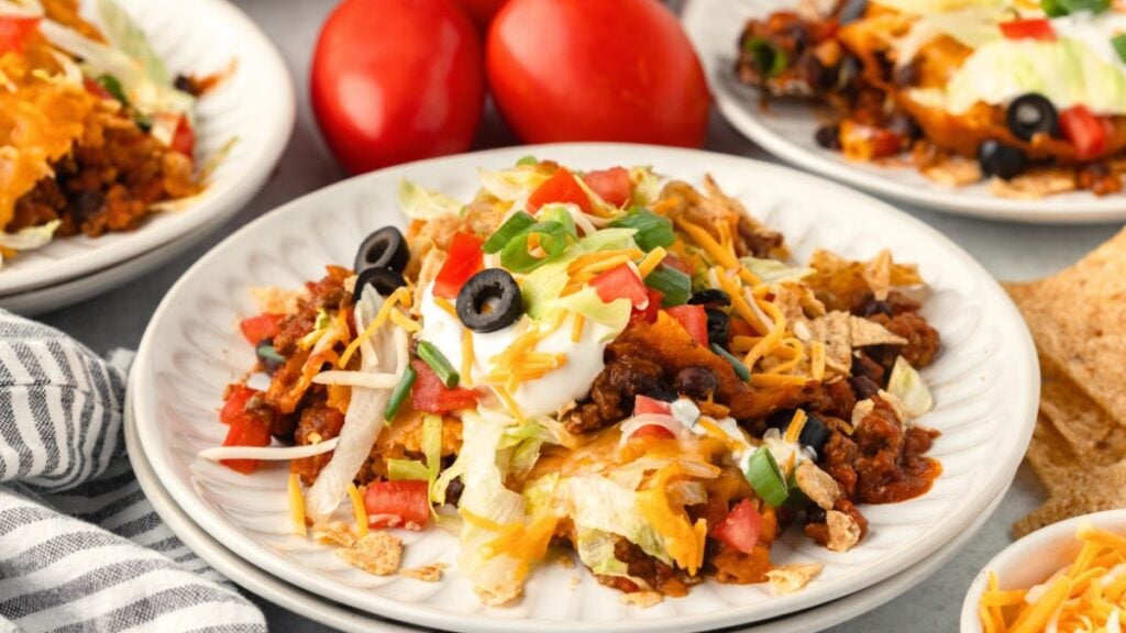 Taco casserole on a white plate garnished with shredded cheese, sour cream and black olives.
