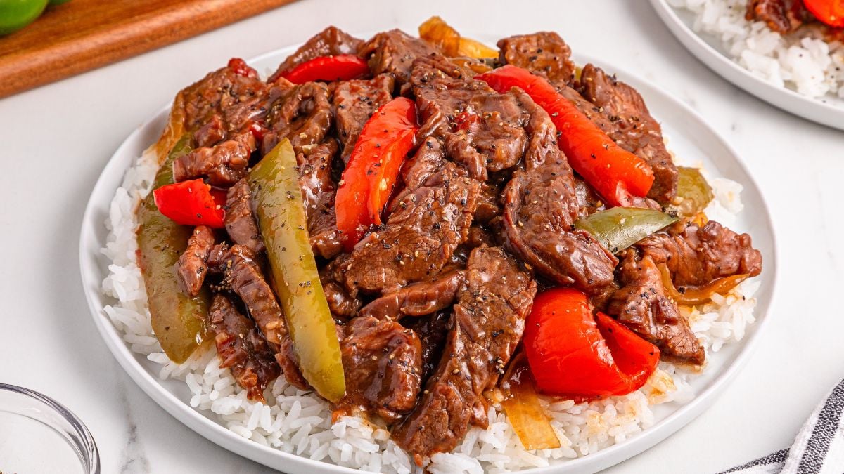 Crockpot pepper steak served on a bed of rice on a plate.