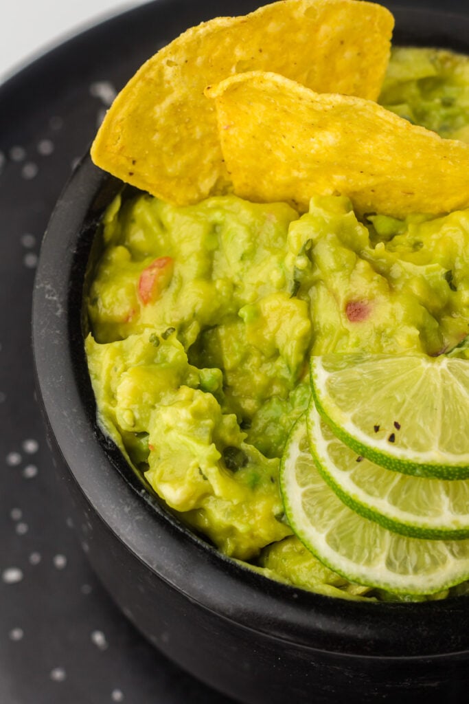 Guacamole dip in a black pole with sliced limes.