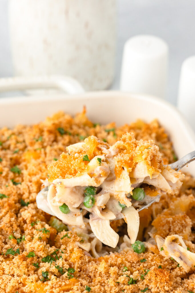 A fork lifting a bite of tuna noodle casserole out of the dish.