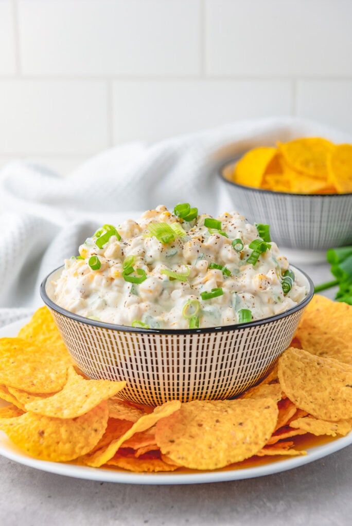 Crack corn dip in a bowl with tortilla chips on the side.