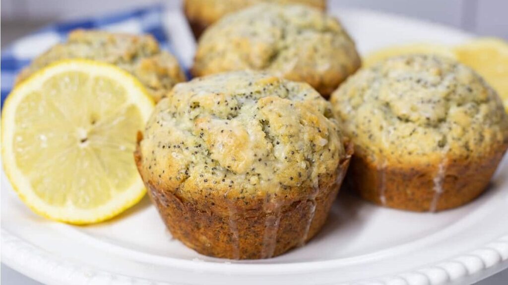 Lemon poppyseed muffins on a white plate with fresh lemon garnish to the side.