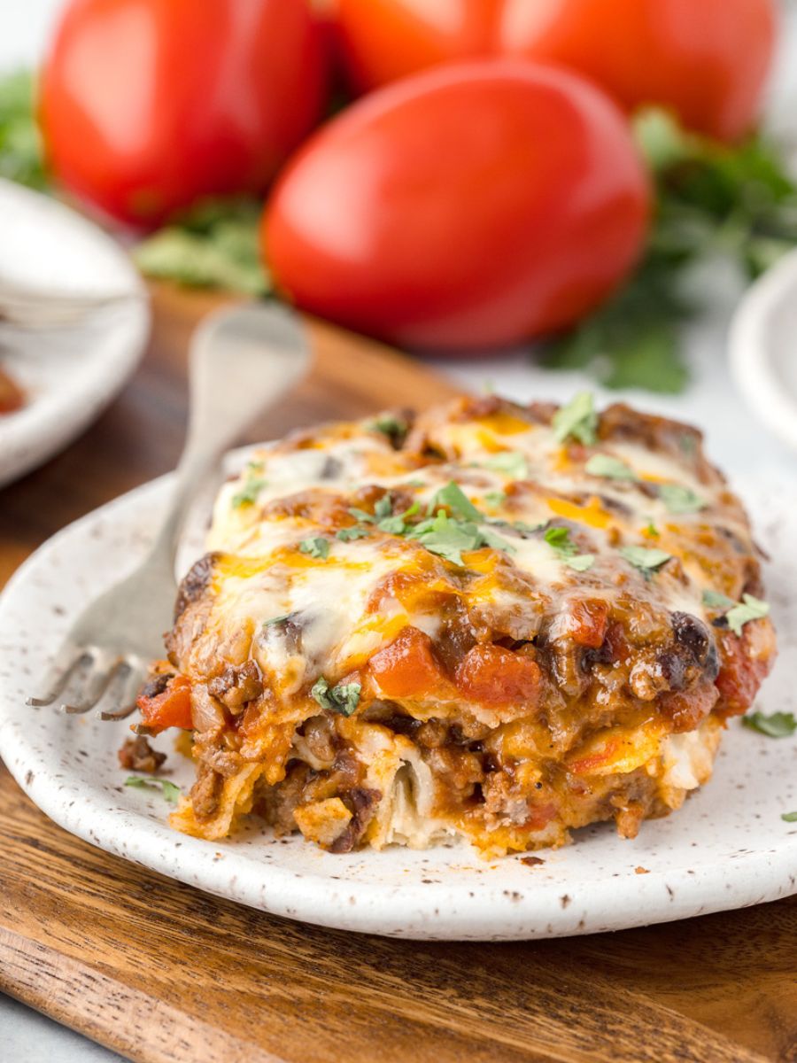 Beef enchilada casserole served on a plate with fresh tomatoes in the background.
